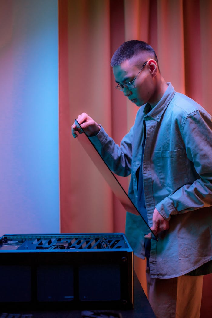 Asian man repairing a PC indoors with colorful lighting, focused on installing components.